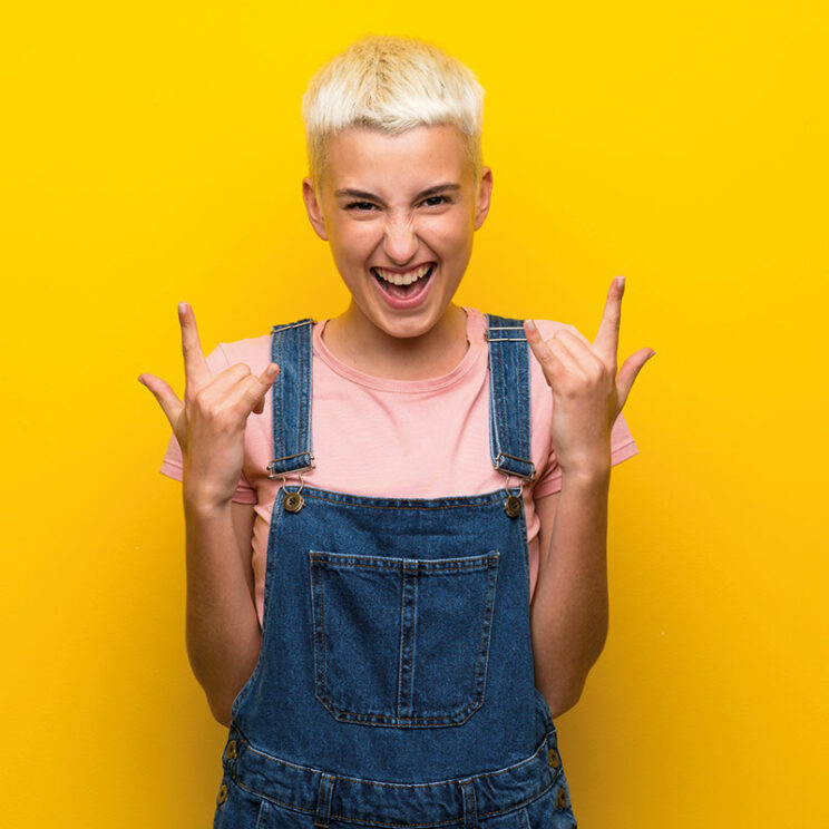 Bild zeigt eine gut gelaunte junge Frau. Sie steht vor einer gelben Wand.