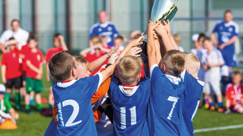 Bild zeigt Kinder in Fussballkleidung. Sie halten einen Pokal hoch.