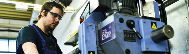 Bild zeigt einen Mitarbeiter der Werkstatt. Er steht an einer großen Maschine.
