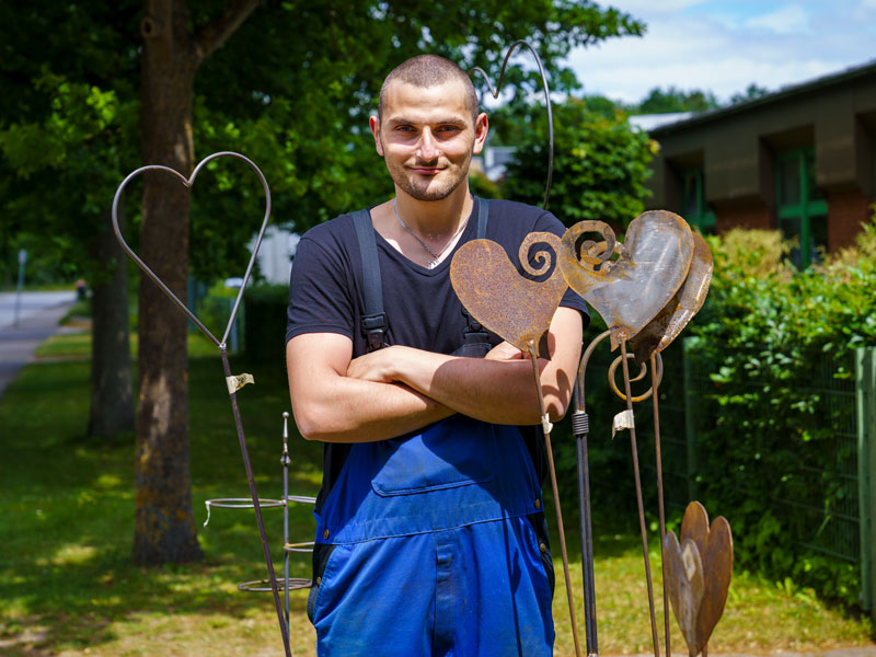 Bild zeigt Mann zwischen Gartendeko aus Metall