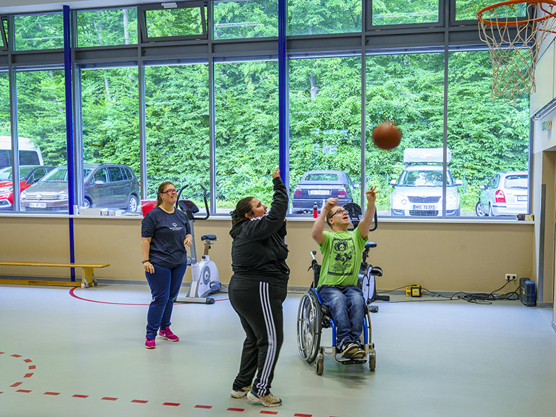 Bild zeigt 2 Frauen und einen Rollstuhlfahrer beim Basketball